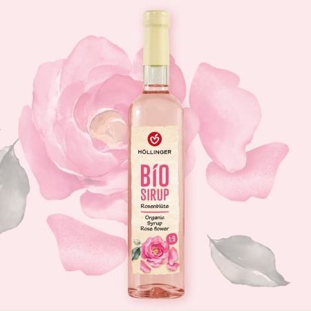 Eine Flasche Höllinger Bio-Sirup Rosenblüte vor einem Hintergrund mit rosa Blütenblättern