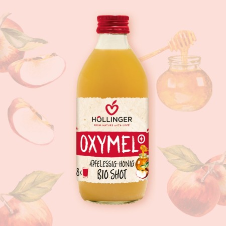 Höllinger Oxymel+ Apfelessig Honig Bio Shot in der 330ml Glasflasche vor einem Hintergrund aus Äpfeln und Honig.