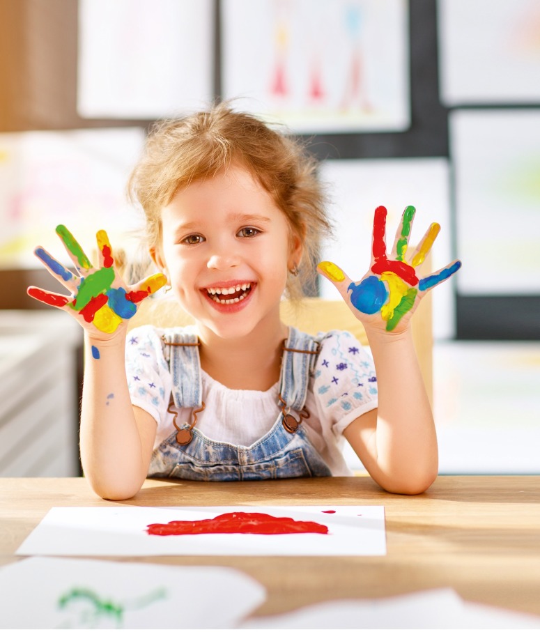 Lächelndes Kind mit farbenfroh bemalten Händen zeigt kreative Freude beim Malen