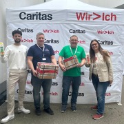 Vier Personen vor Caritas-Stand mit Hollinger Saftpackungen und Webshop-Kartons.